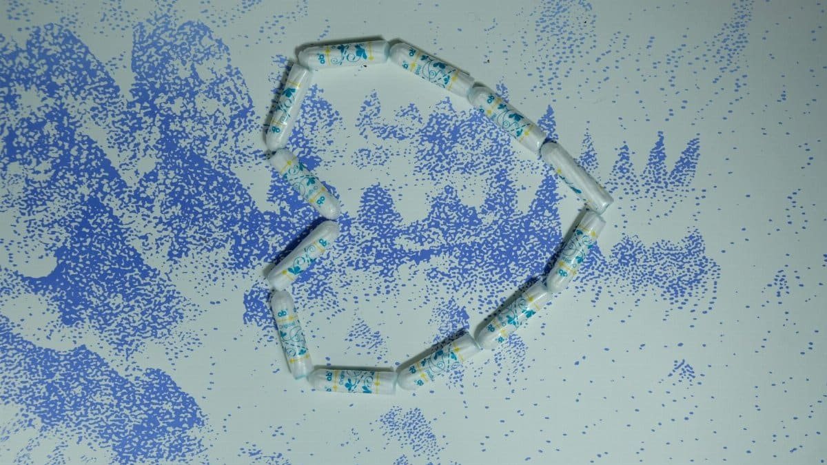 Top view of soft cotton tampons placed in shape of hear on white table surface with blue blots