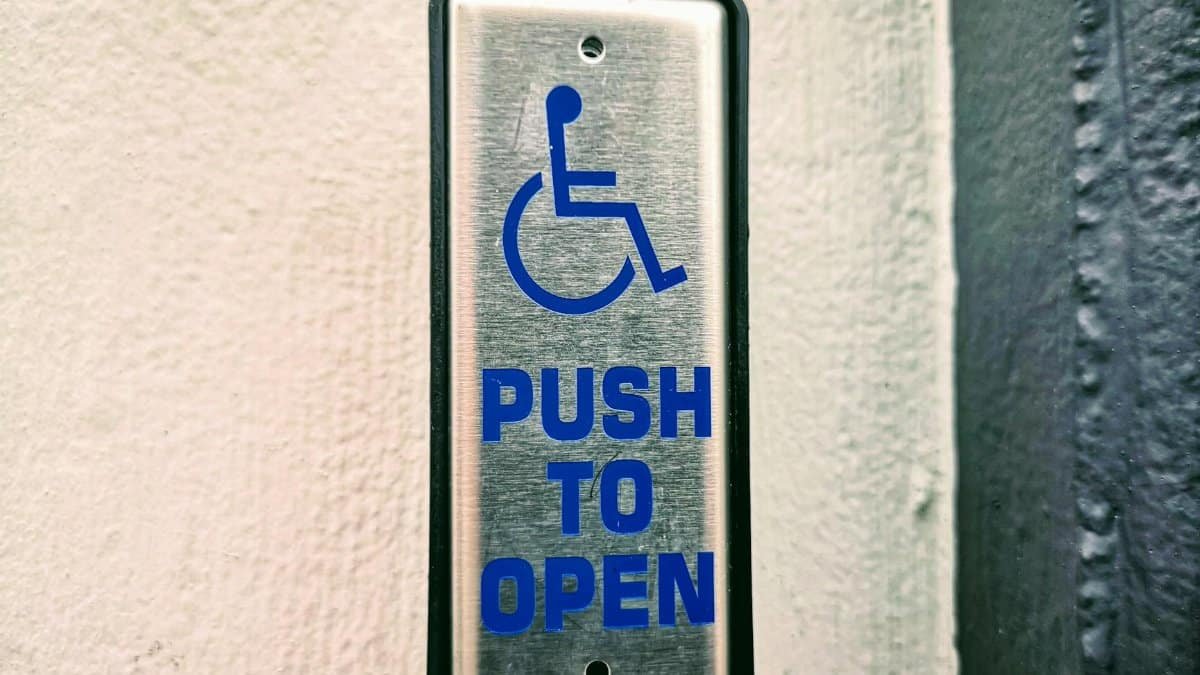 Close-up of a push button sign for accessibility on a white wall.
