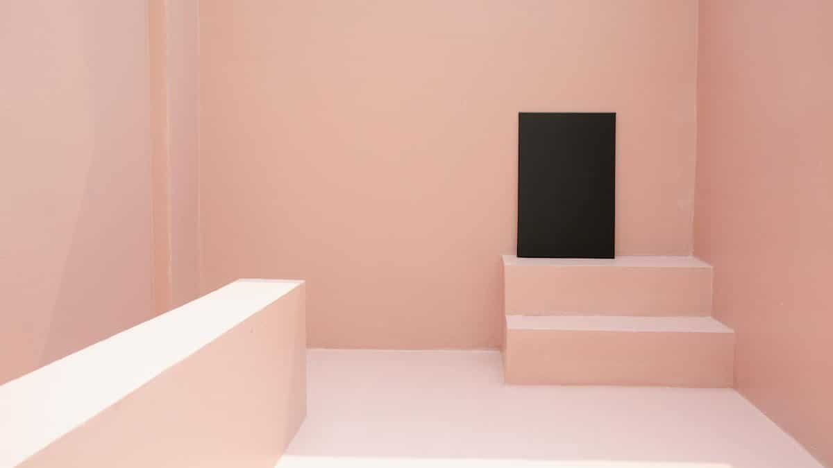 A modern minimalist pink room featuring a black canvas on small steps.