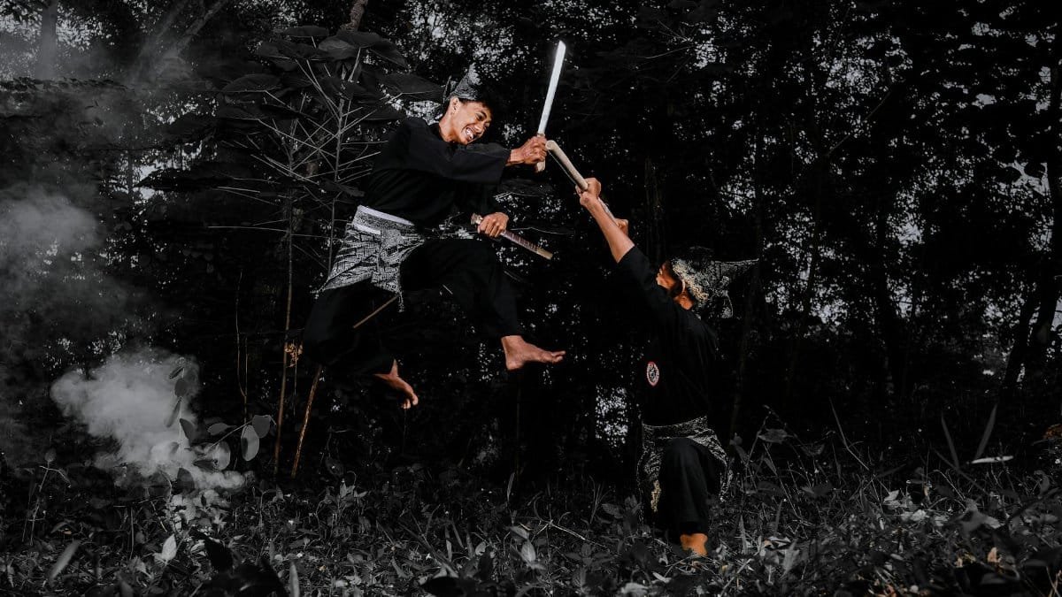 Two martial artists engaged in a high-flying sword fight in a dense forest.