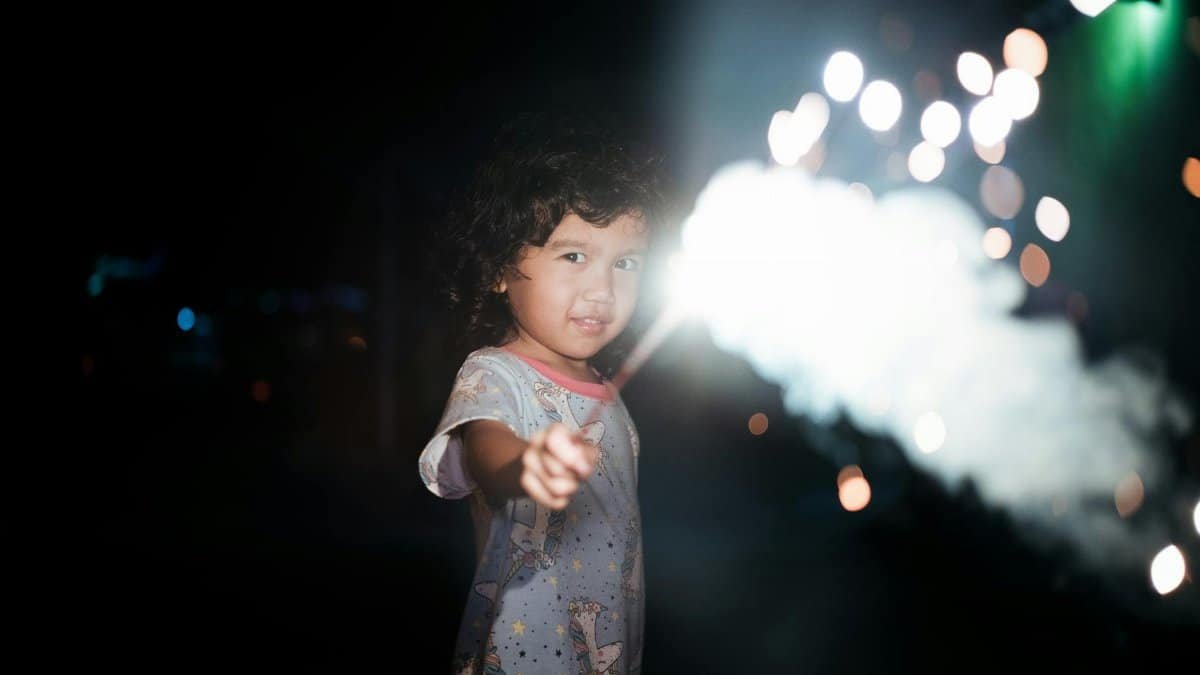 A young girl with a sparkler in hand lights up the night with joy and wonder.