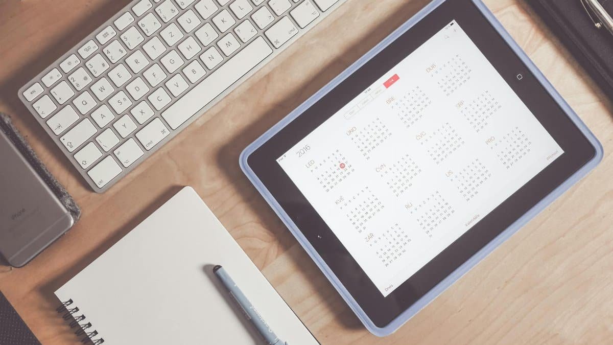 A tidy desk setup featuring a tablet displaying a calendar, keyboard, and stationary items.