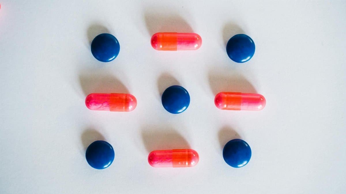Various blue and pink pills and capsules arranged on a white background, showcasing medication.