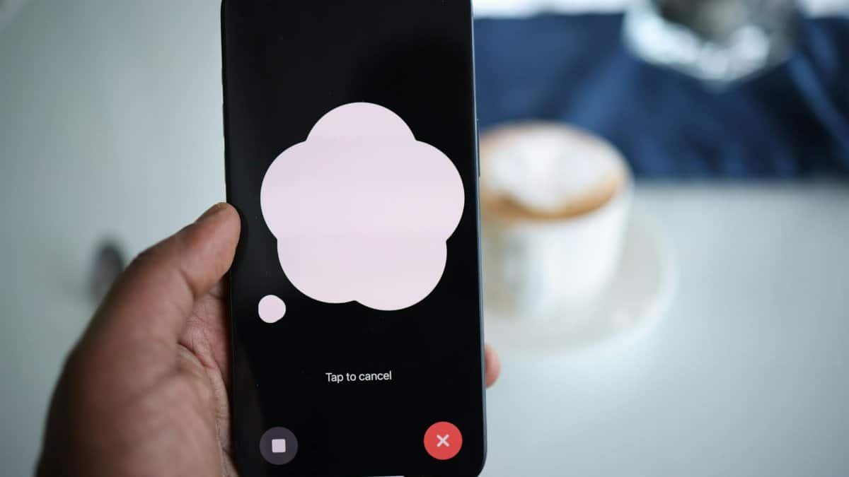 Close-up of a smartphone in hand with AI voice chat bubble and coffee in background.