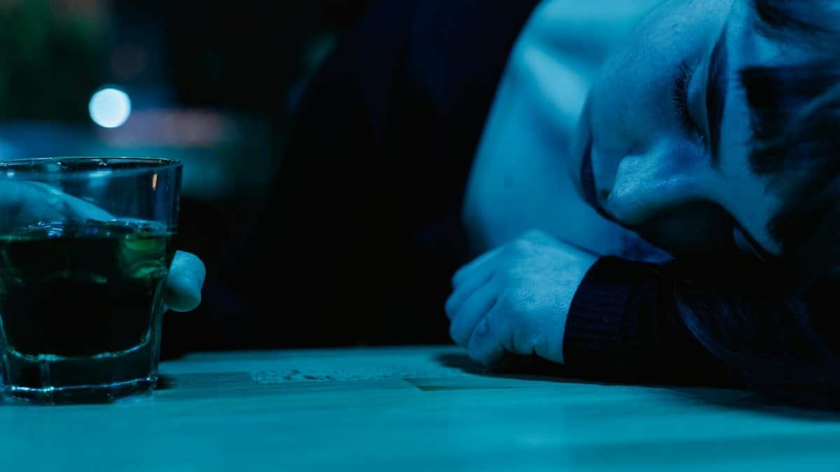 A woman rests on a table next to a glass of drink, illuminated in blue light.