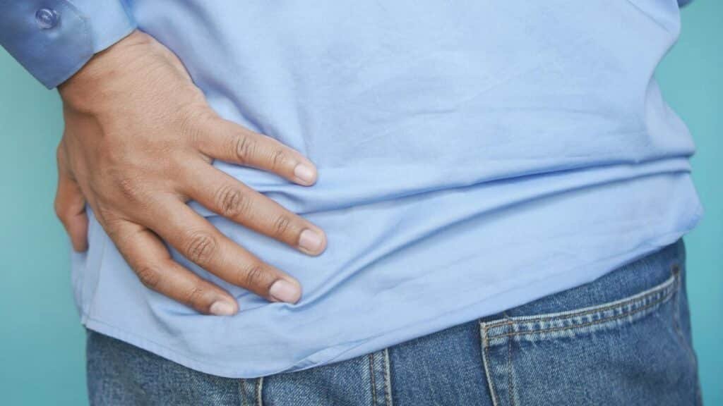 A person in a blue shirt and jeans clutching their hip, possibly indicating pain.