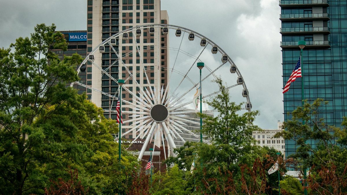 View of the SkyView Atlanta Ferris wheel against the city skyline and lush greenery, featuring American flags.