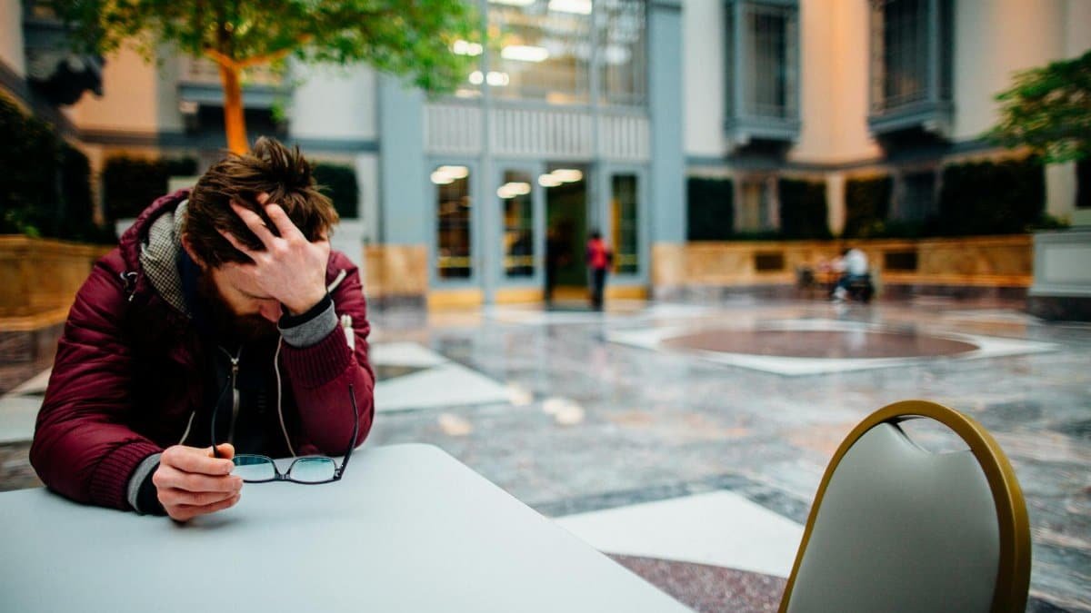 Man holding eyeglasses in hand, showing stress in a modern indoor atrium.