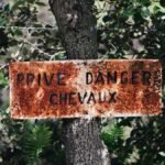An old French warning sign on a tree amidst lush greenery, indicating danger and private property.