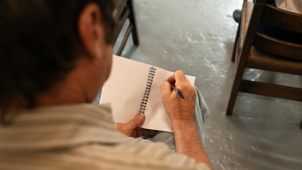 Close-up of a man writing in a notebook indoors, capturing a candid moment.