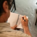 Close-up of a man writing in a notebook indoors, capturing a candid moment.