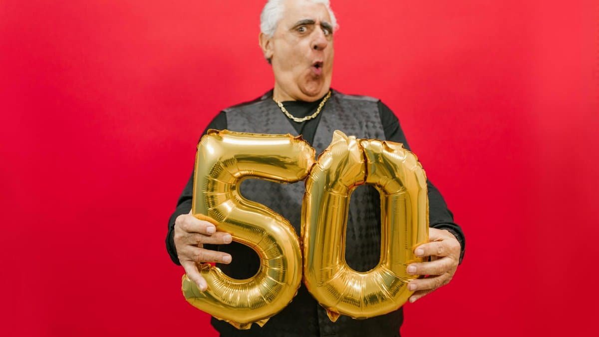 A joyful senior holding gold '50' balloons against a vibrant red backdrop.