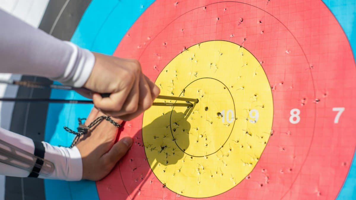 An archer retrieves arrows from a colorful archery target during a sunny day outdoors.
