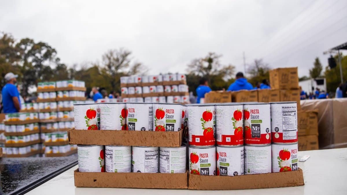 Volunteers at a community food drive organizing canned goods for distribution outdoors.