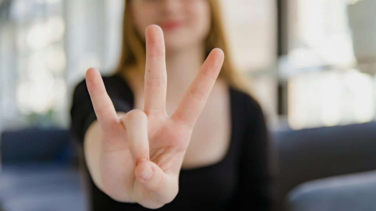 A close-up image of a woman making the ASL sign for 'I Love You' with focus on the hand gesture.