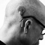 Black and white profile of a man wearing glasses and a hearing aid, studio shot.