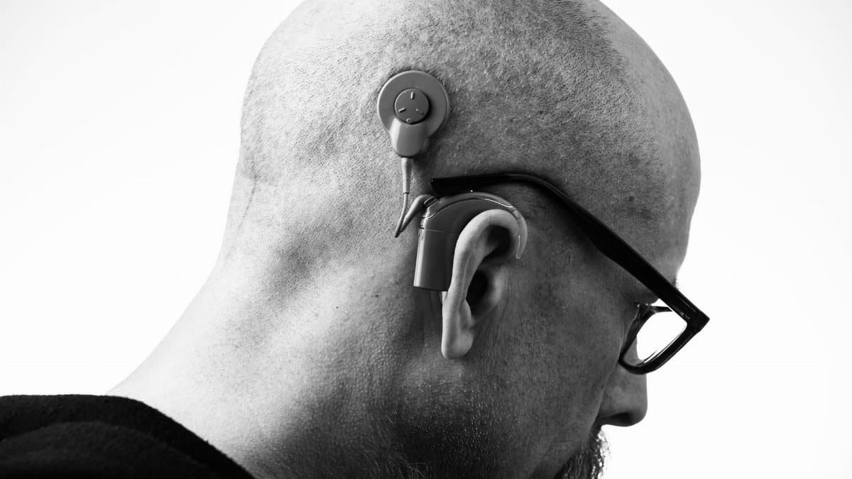 Black and white profile of a man wearing glasses and a hearing aid, studio shot.
