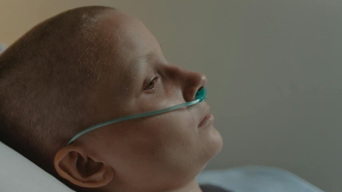 A bald woman with nasal cannula lying down, reflecting illness and solitude.