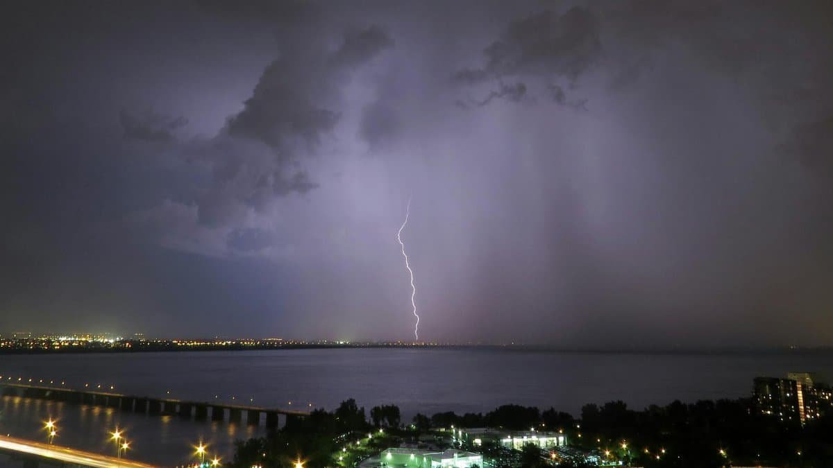 Dramatic scene capturing a lightning strike over a city with a reflection on the water at night.