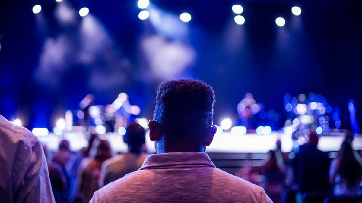 Back view of a diverse audience enjoying a live concert under stage lights indoors.