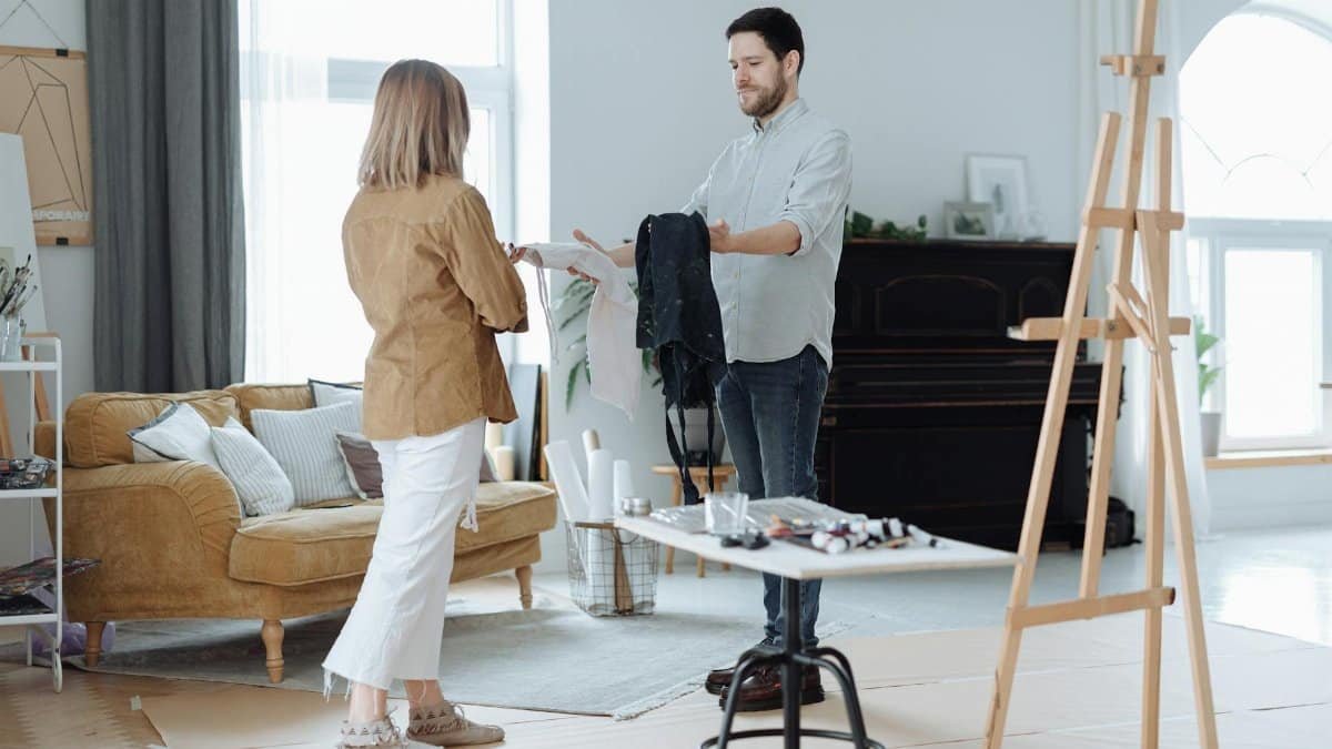 Two artists collaborating in a bright studio with various art supplies and an easel.