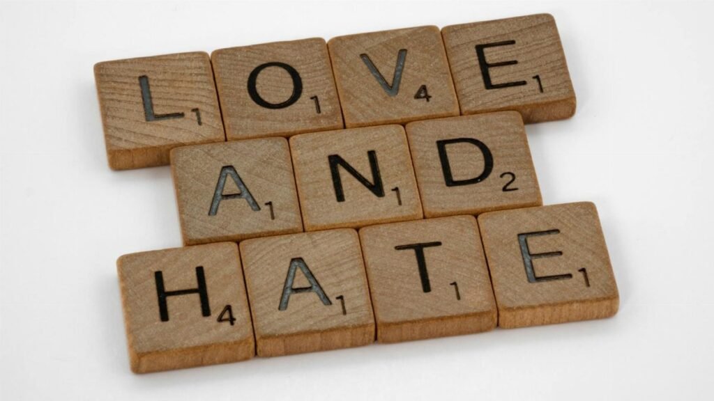 Close-up of wooden Scrabble tiles spelling 'Love and Hate' on a white background, symbolizing contrasting emotions.