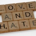 Close-up of wooden Scrabble tiles spelling 'Love and Hate' on a white background, symbolizing contrasting emotions.