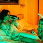 Stylish young couple in bed with retro camera and bunny ears, creating a vintage vibe.