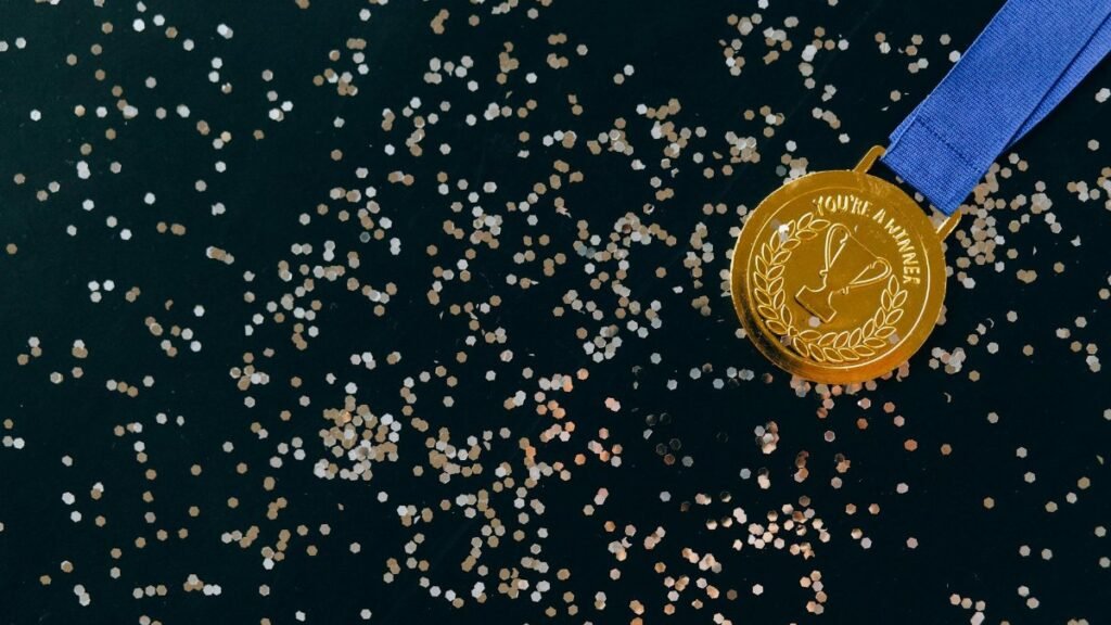 Close-up of a gold medal with blue ribbon and confetti on a black surface, symbolizing victory.