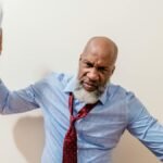 A bald man in a blue shirt expresses anger by throwing papers indoors.