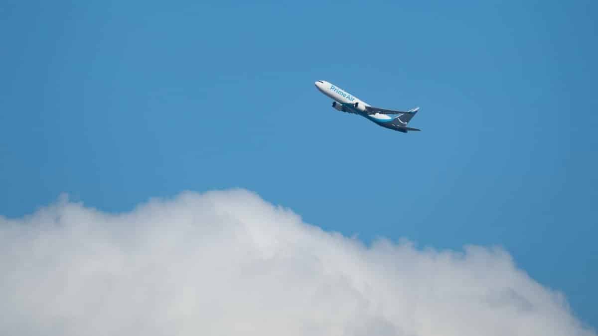A commercial airplane from Prime Air flying high above fluffy clouds against a clear blue sky.