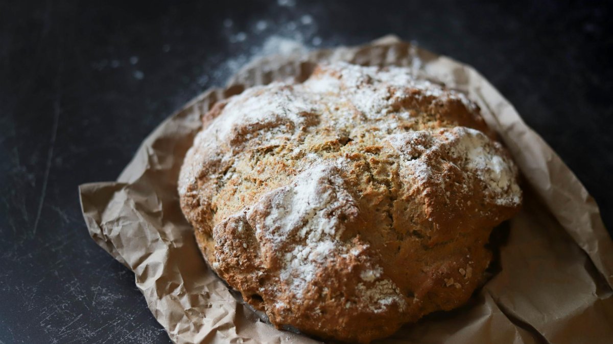 A rustic, freshly baked sourdough bread loaf on brown paper with a dark textured background.