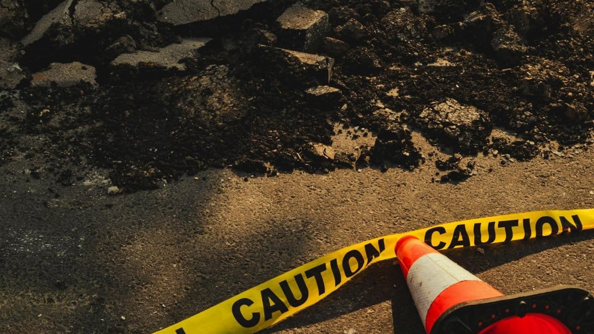 Broken sidewalk with rubble, caution tape, and traffic cone in urban construction site.