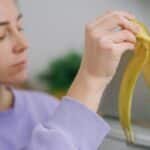 Close-up of a woman throwing a banana peel into a trash bin. Eco-friendly waste management.
