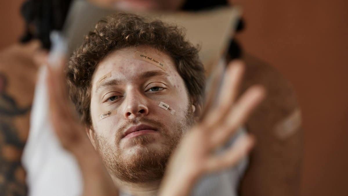 Close-up of a bearded man with band-aids reflecting in a broken mirror, conveying introspection.