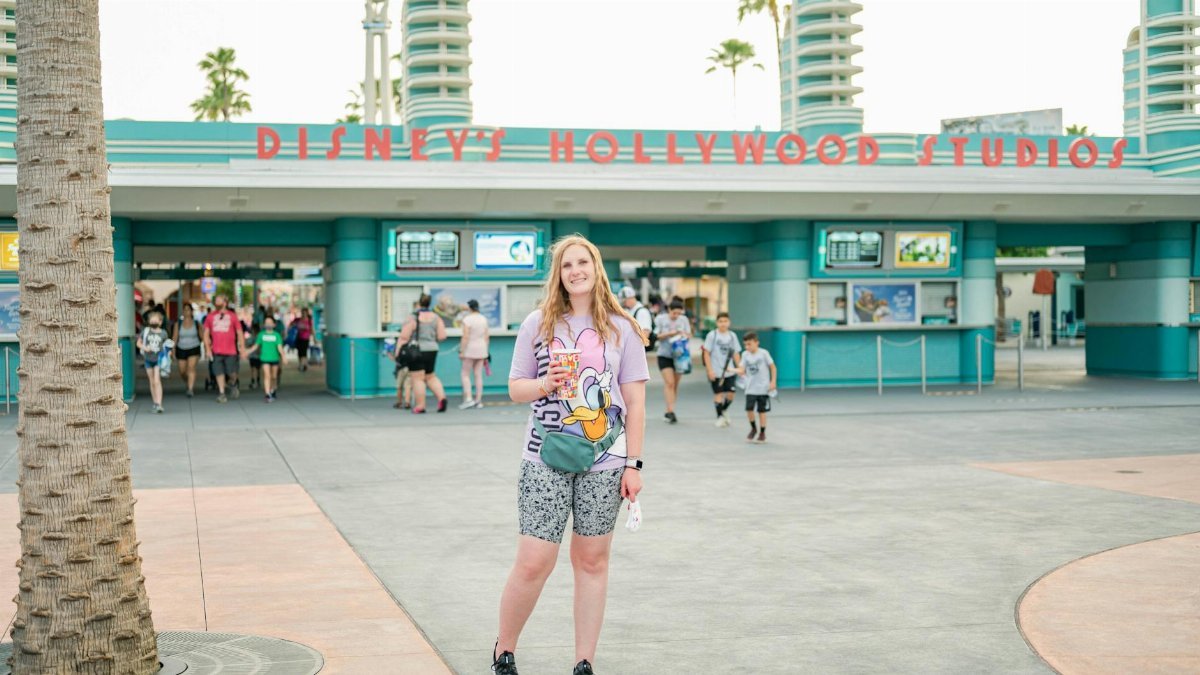 Woman smiling in front of Disney's Hollywood Studios entrance, wearing a Donald Duck shirt.