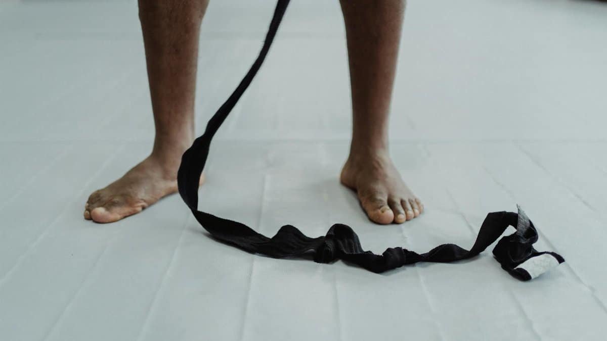 A person stands barefoot on a white mat with martial arts wraps, focusing on strength and balance.