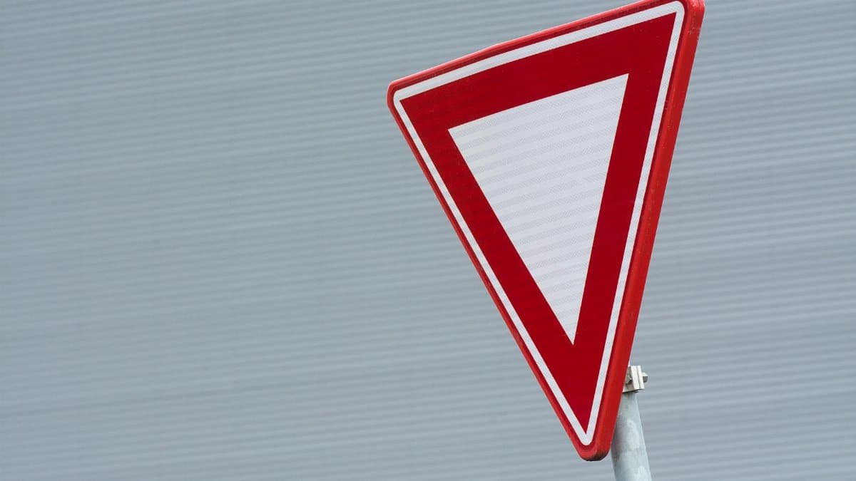 A close-up of a red yield traffic sign against a textured gray background.