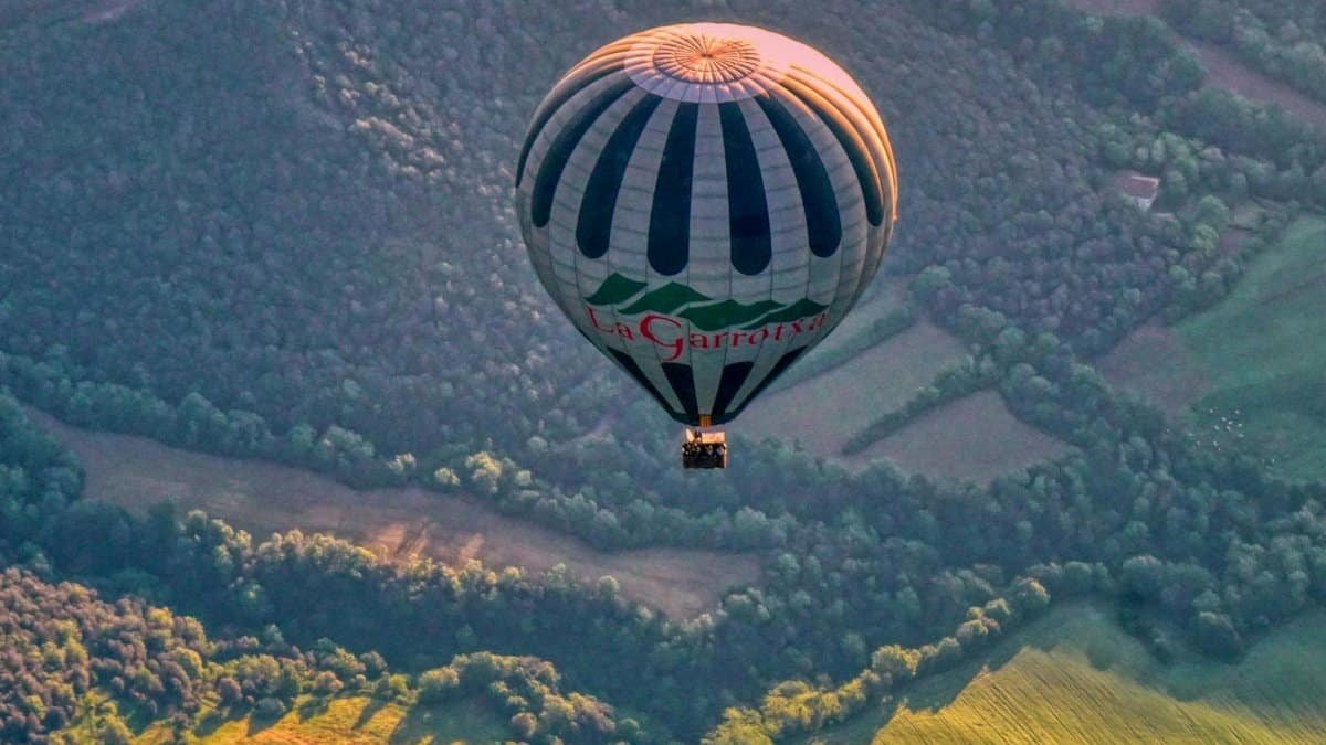 Hot air balloon soaring over lush landscapes of Santa Pau, Catalonia at sunrise.