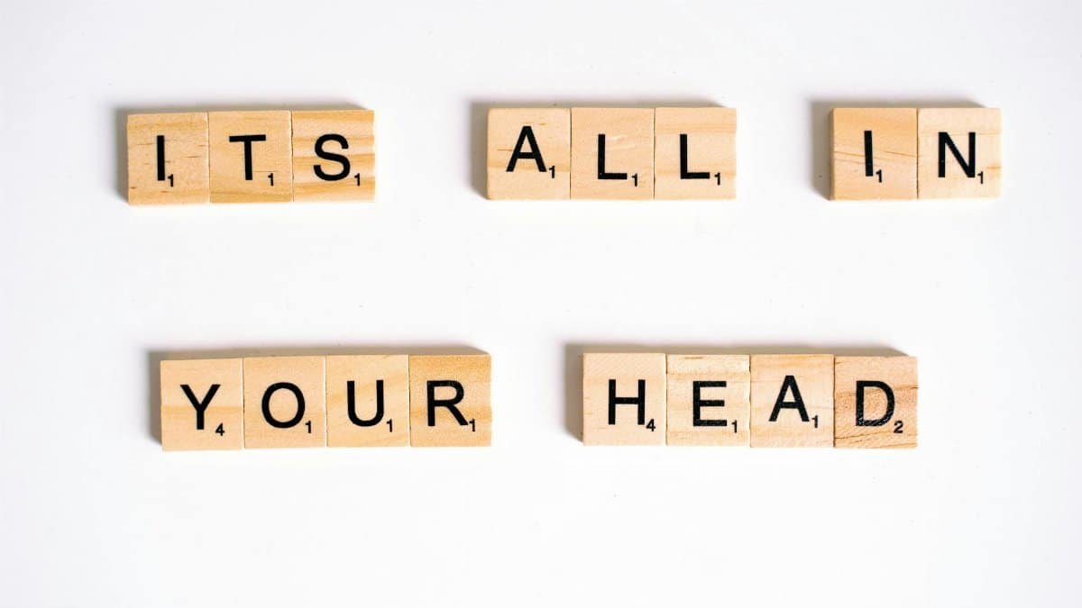 Wooden Scrabble tiles arranged to spell 'ITS ALL IN YOUR HEAD' on a white background.