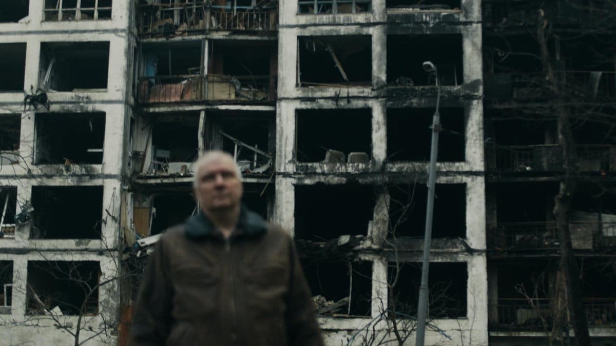 A damaged building in Kyiv, Ukraine with a blurred man in the foreground.