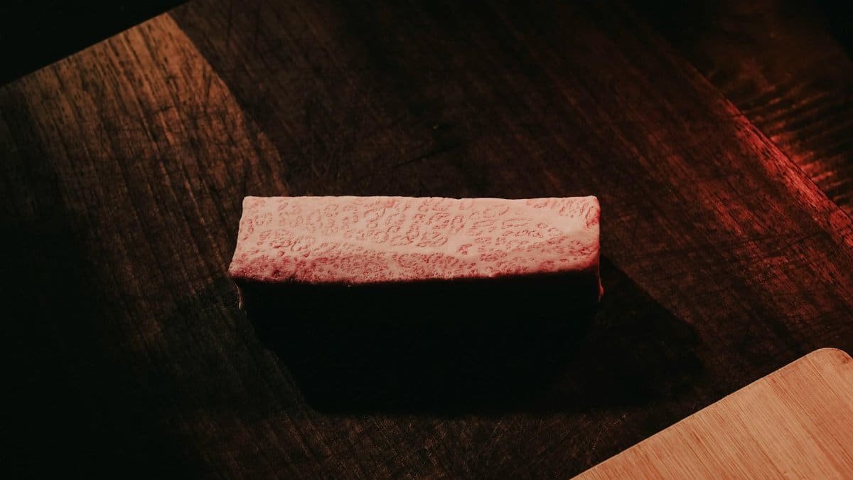 Close-up of marbled Wagyu beef on a rustic dark wooden table, showcasing rich texture and color contrast.