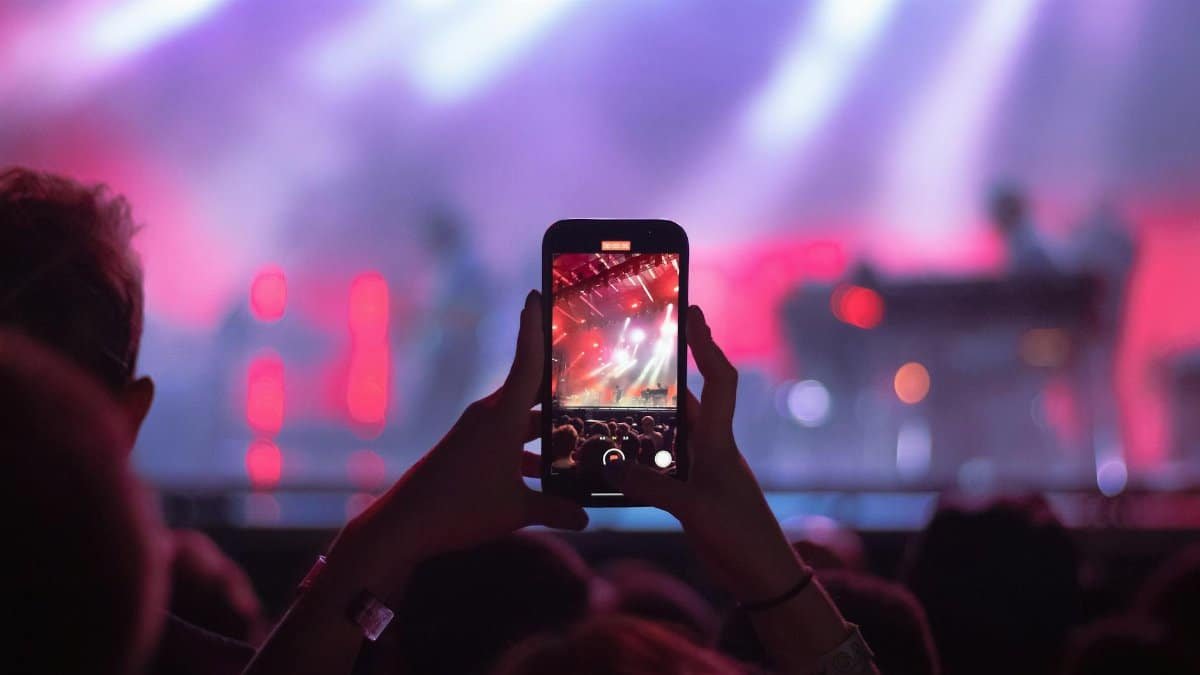 A vibrant concert scene with an audience member recording the performance on a smartphone in Bentonville, AR.