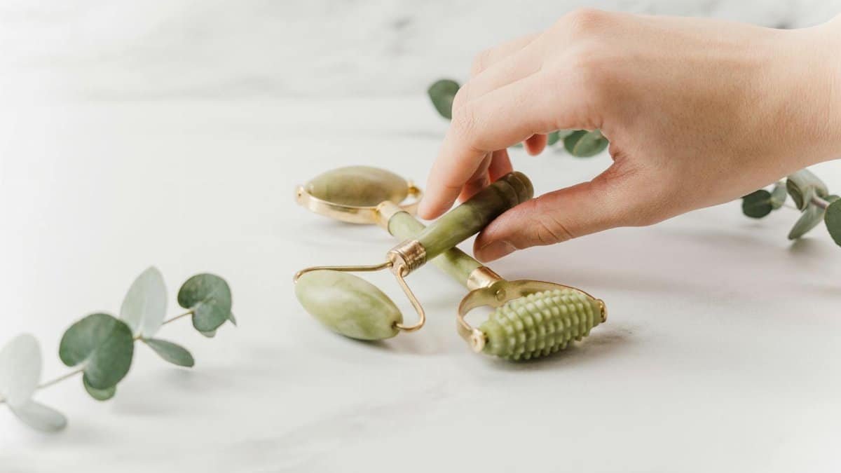 Close-up of a hand holding jade rollers on a marble surface for skincare and wellness.