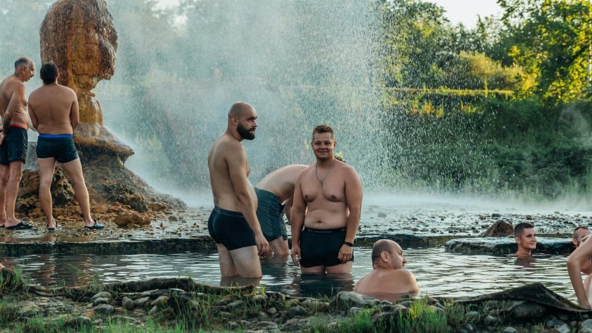 Group of men enjoying natural hot springs outdoors. Steam rises, creating a tranquil scene.