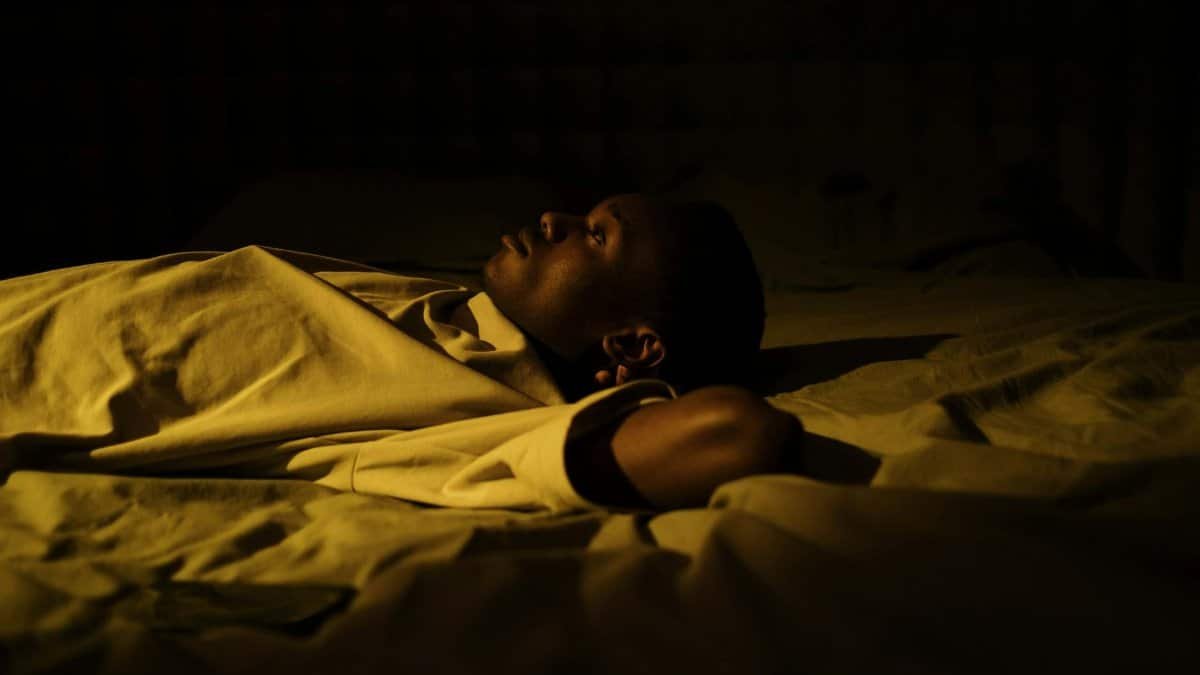 A man struggles with insomnia, lying awake in his dark bedroom at night, reflecting on mental health.