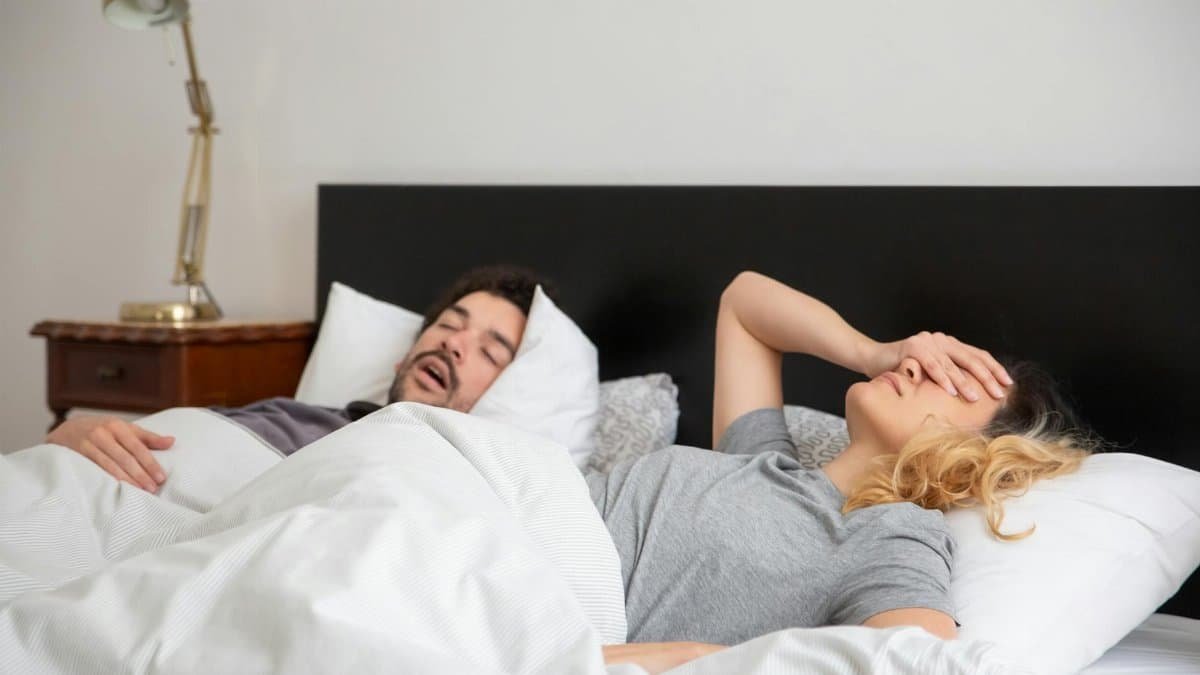A couple in bed, with one partner covering their face due to the other's snoring.