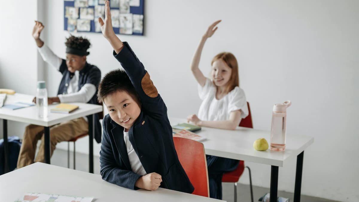 Engaged children in a classroom, eagerly raising hands during a lesson, showcasing diversity and active learning.
