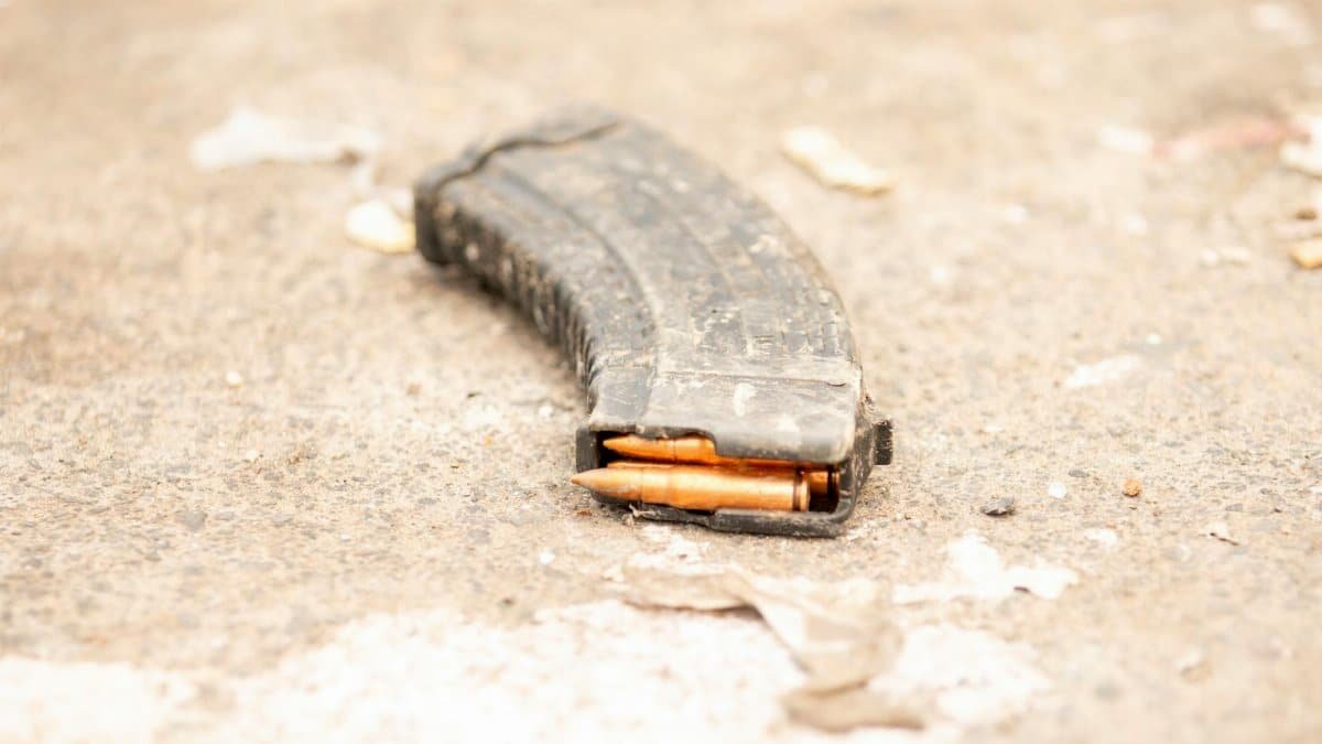 Rifle magazine with visible bullets lying on a rough concrete surface.