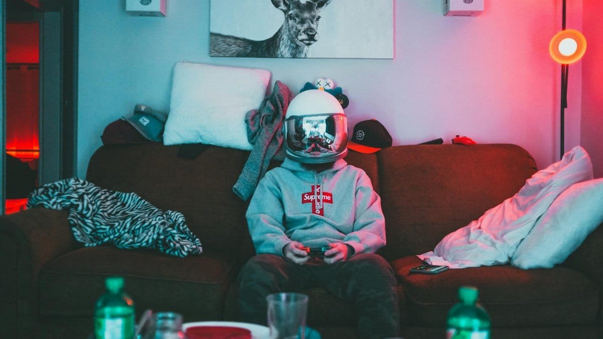 A person wearing a VR helmet, gaming on a couch in a cozy, neon-lit room.